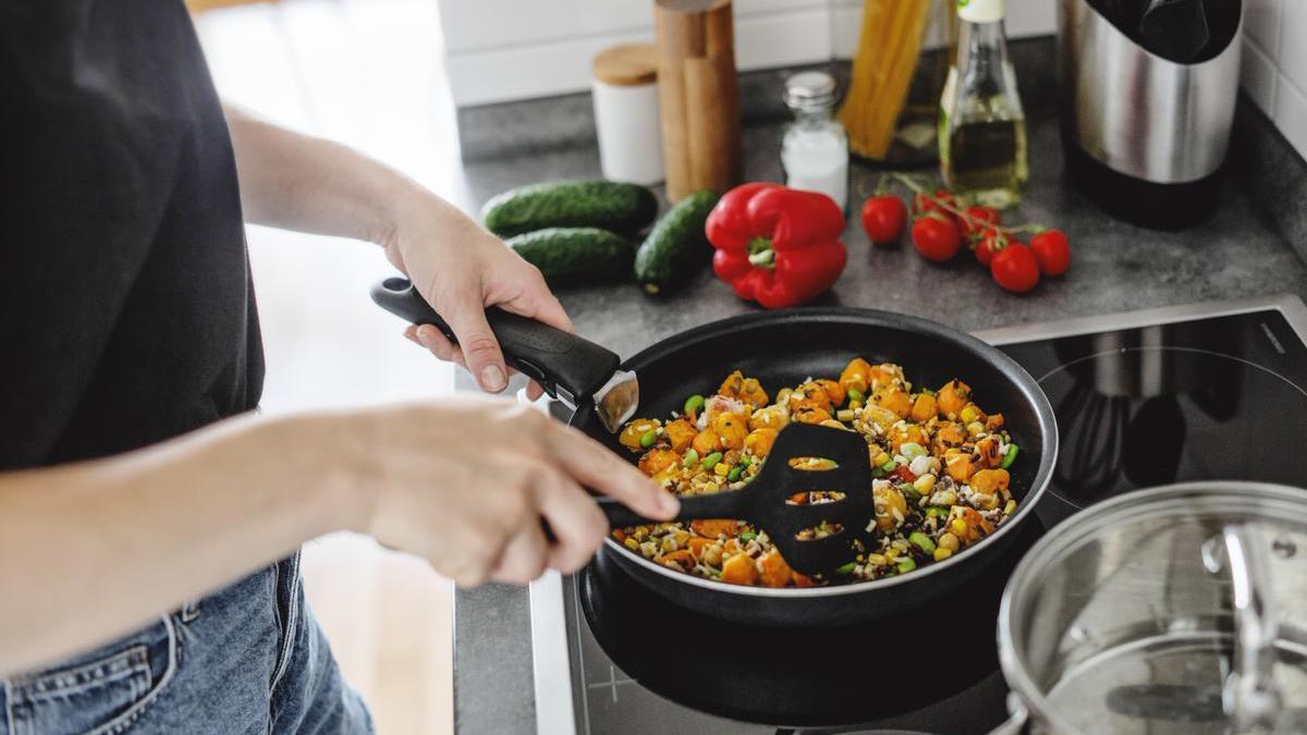 Mujer cocina verduras frescas en una sartén en casa.