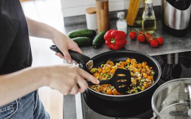 Mujer cocina verduras frescas en una sartén en casa.