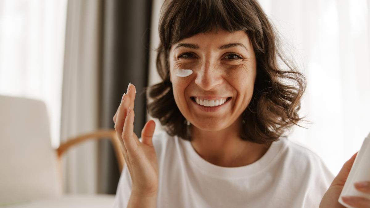 Mujer aplica protector solar facial en casa antes de exponerse al sol.