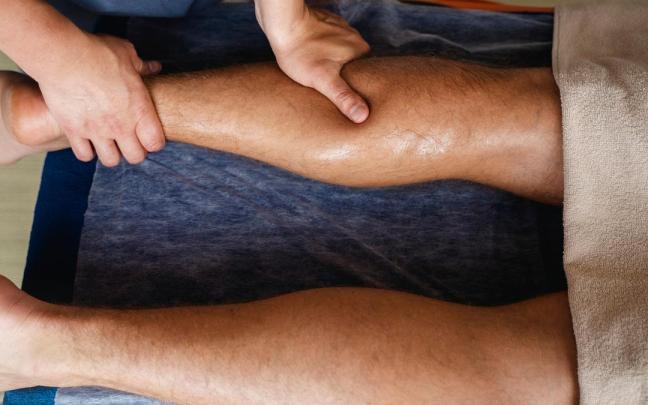 Un fisioterapeuta realiza un masaje en el gemelo a un paciente.