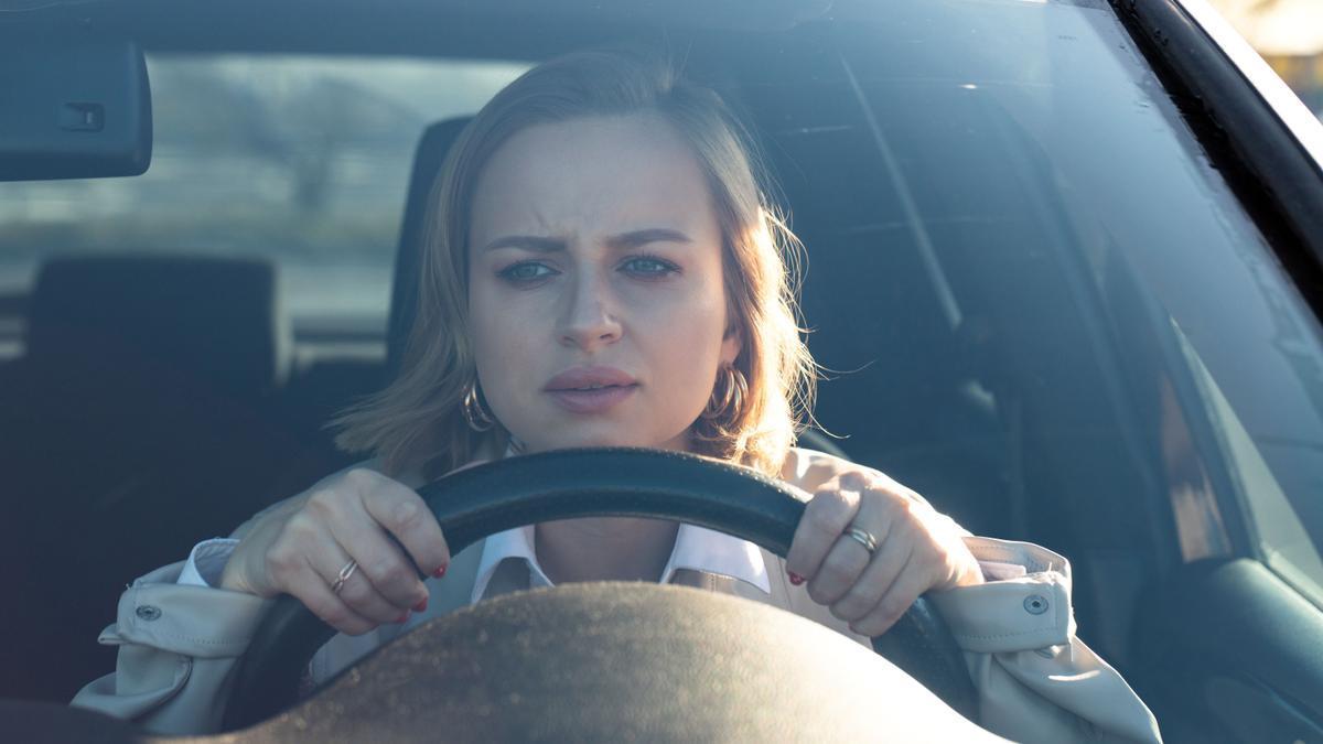 Una mujer conduce su coche con rostro inquieto.