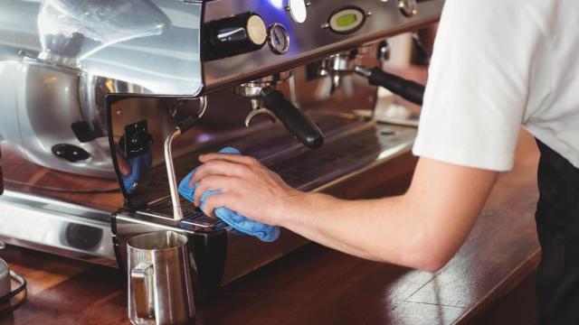 Una camarera limpia la cafetera de un bar.