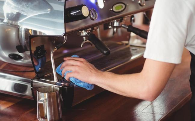 Una camarera limpia la cafetera de un bar.