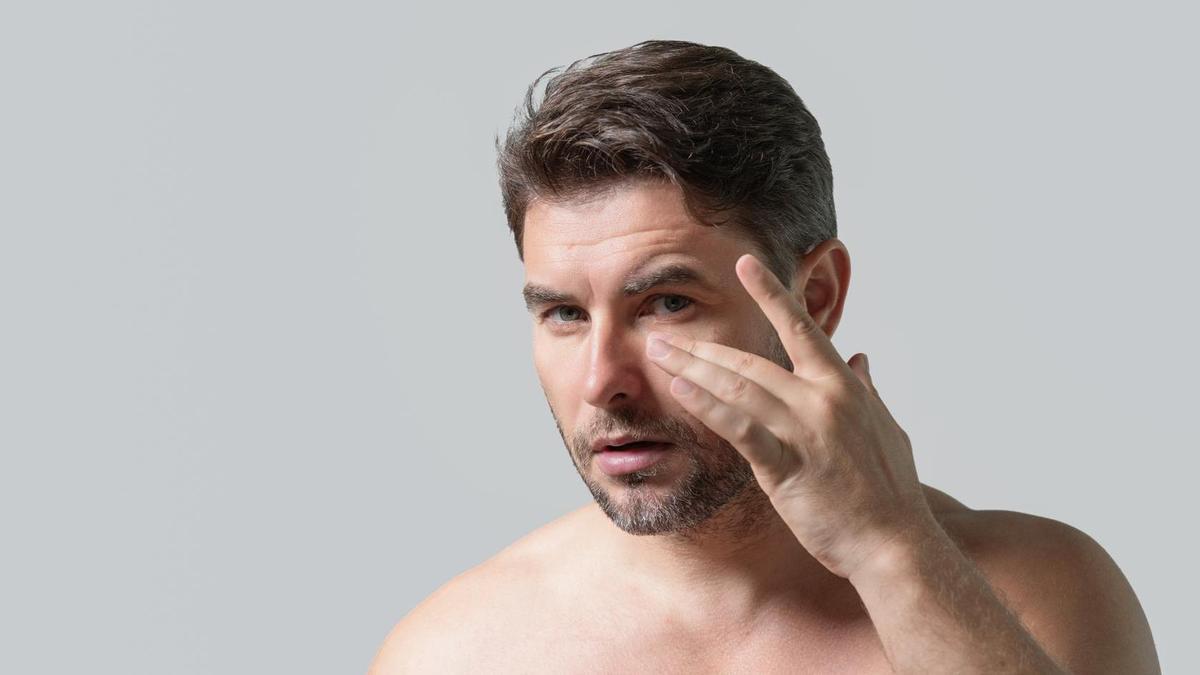 Un hombre se aplica un bálsamo para las arrugas ante un espejo.