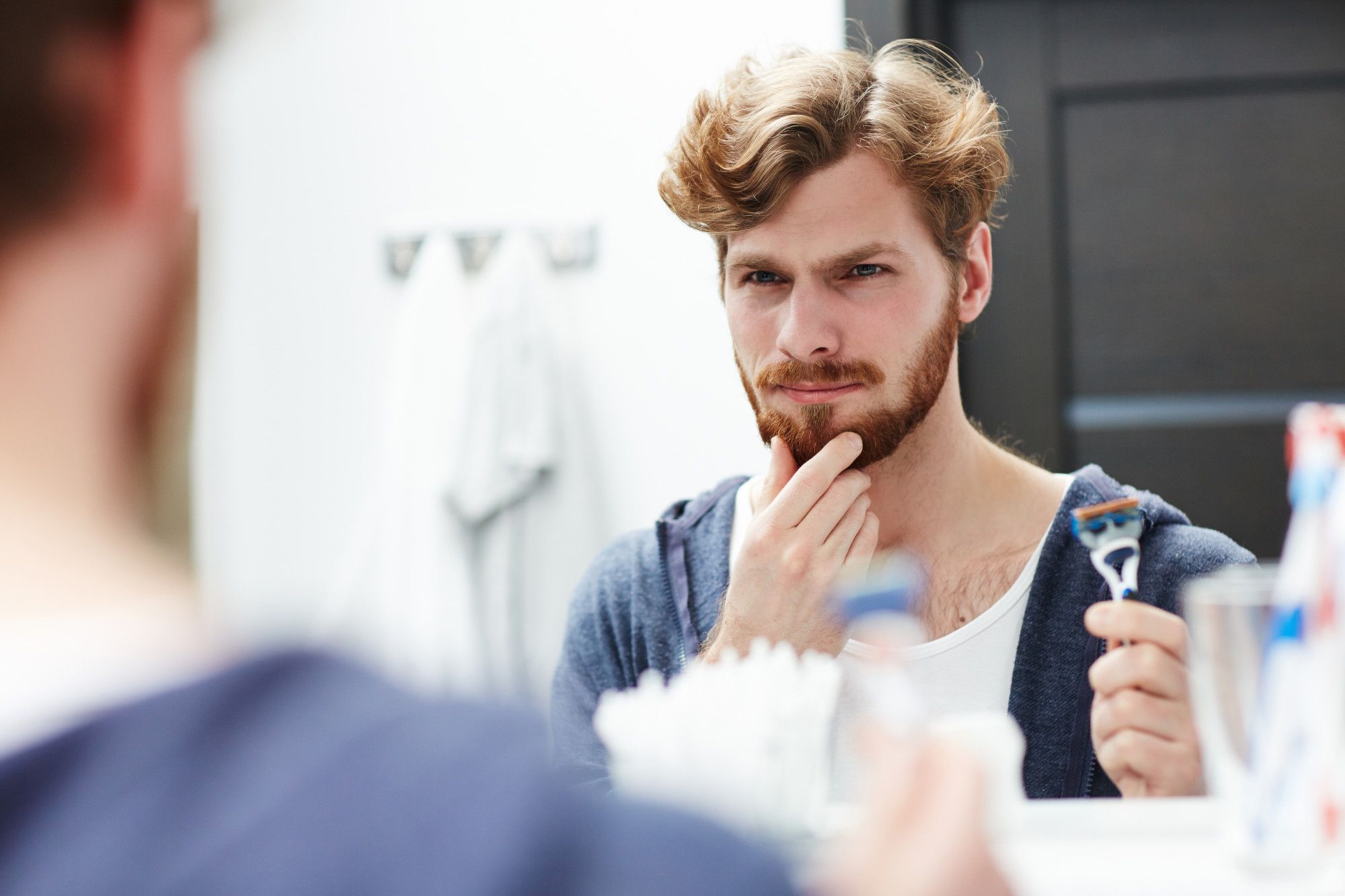 Un hombre se mira la barba en el espejo antes de afeitarse.