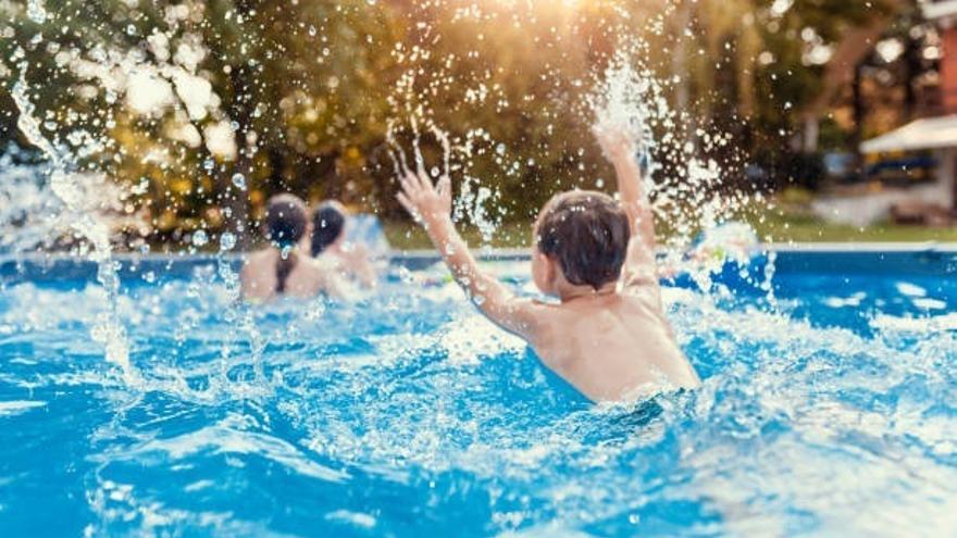Tres menores disfrutan de un baño en una piscina durante un caluroso día de verano.