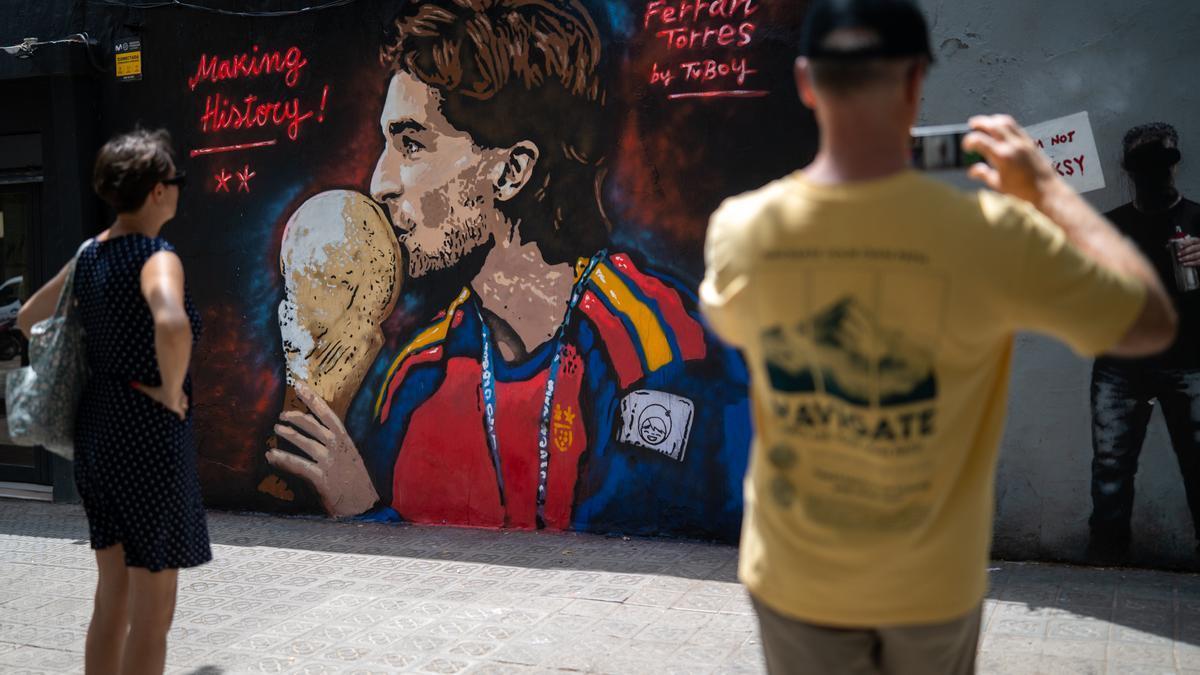 Varias personas pasan por delante del mural de Ferran Torres del artista urbano Tvboy.