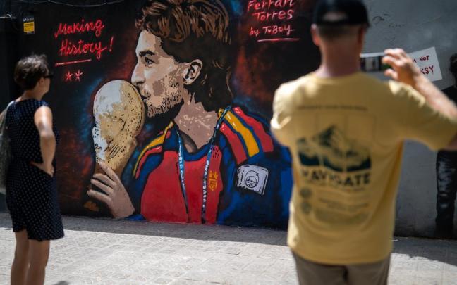 Varias personas pasan por delante del mural de Ferran Torres del artista urbano Tvboy.