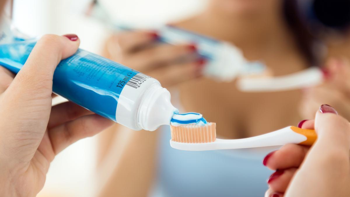 Manos de una persona añadiendo pasta de dientes al cepillo