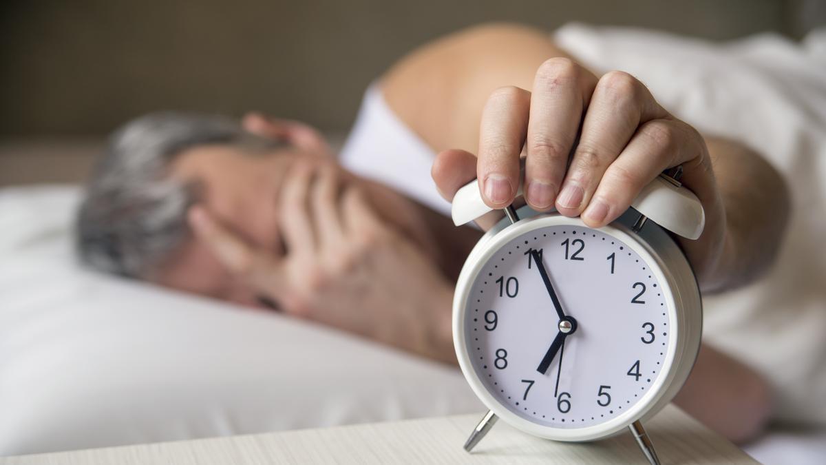 Señor recién levantado coge el reloj que hay encima de la mesilla de noche.