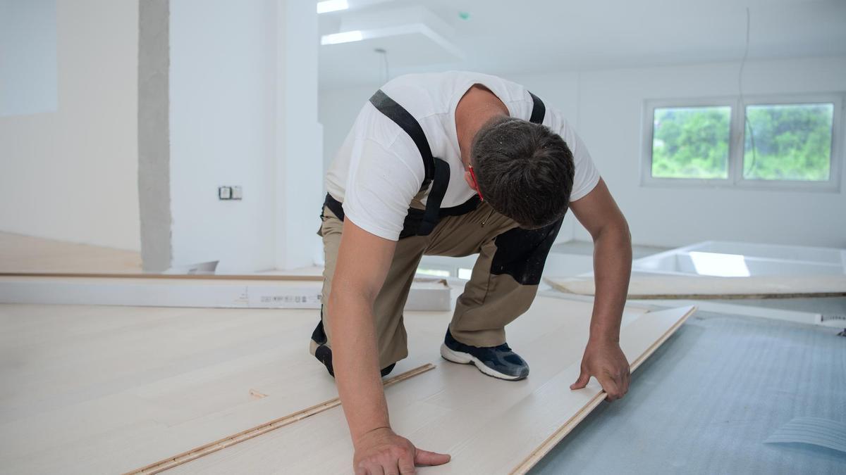 Un carpintero coloca el suelo en una vivienda.