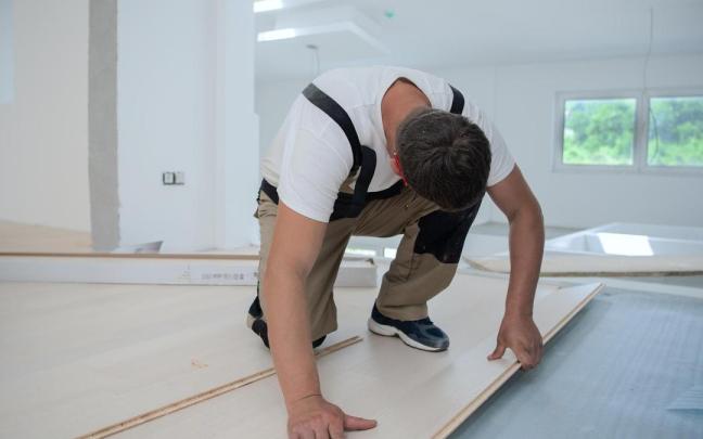 Un carpintero coloca el suelo en una vivienda.