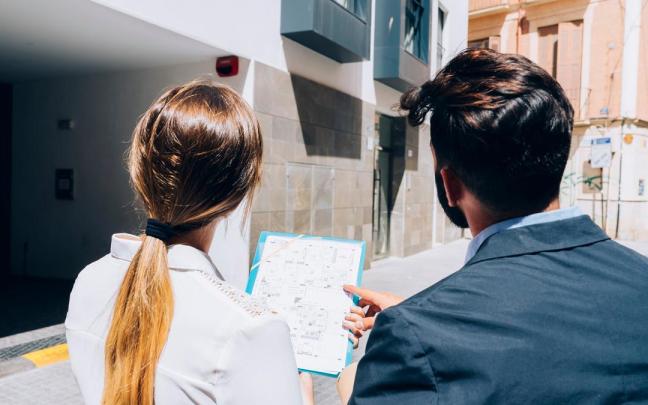Una pareja contempla los planos de un piso junto a un edificio.