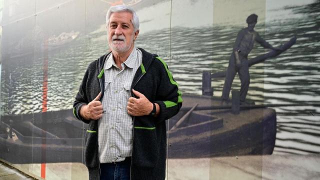 Josu Chueca ante un mural con paisajes de la guerra sobre un fondo de la ría de Bilbao.