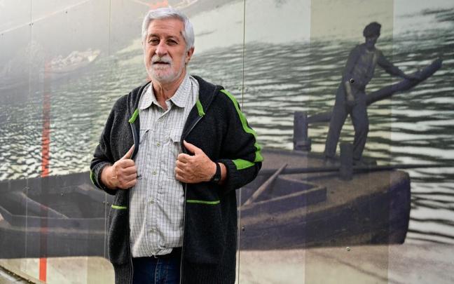 Josu Chueca ante un mural con paisajes de la guerra sobre un fondo de la ría de Bilbao.
