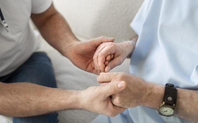 Un sanitario sujeta la mano de un paciente.