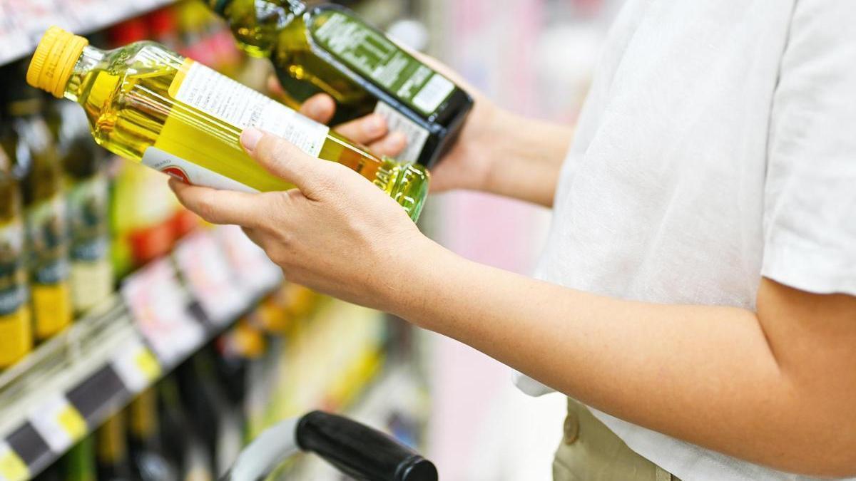 Una mujer, con dos botellas de aceite de oliva en un supermercado.