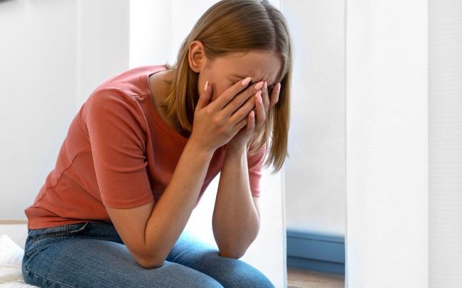 Una mujer, de bajón, sentada en la cama.