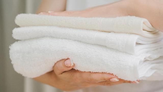 Mujer sostiene unas toallas blancas limpias y recién dobladas.