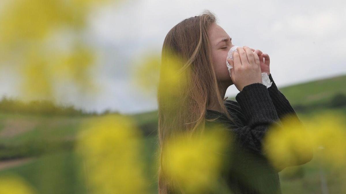 Una joven se tapa la nariz con un pañuelo mientras estornuda.
