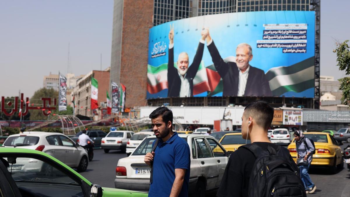 Iraníes pasan ante una valla publicitaria que representa al presidente iraní Masoud Pezeshkian (d) y al fallecido líder de Hamás, Ismail Haniyeh, en Teherán.