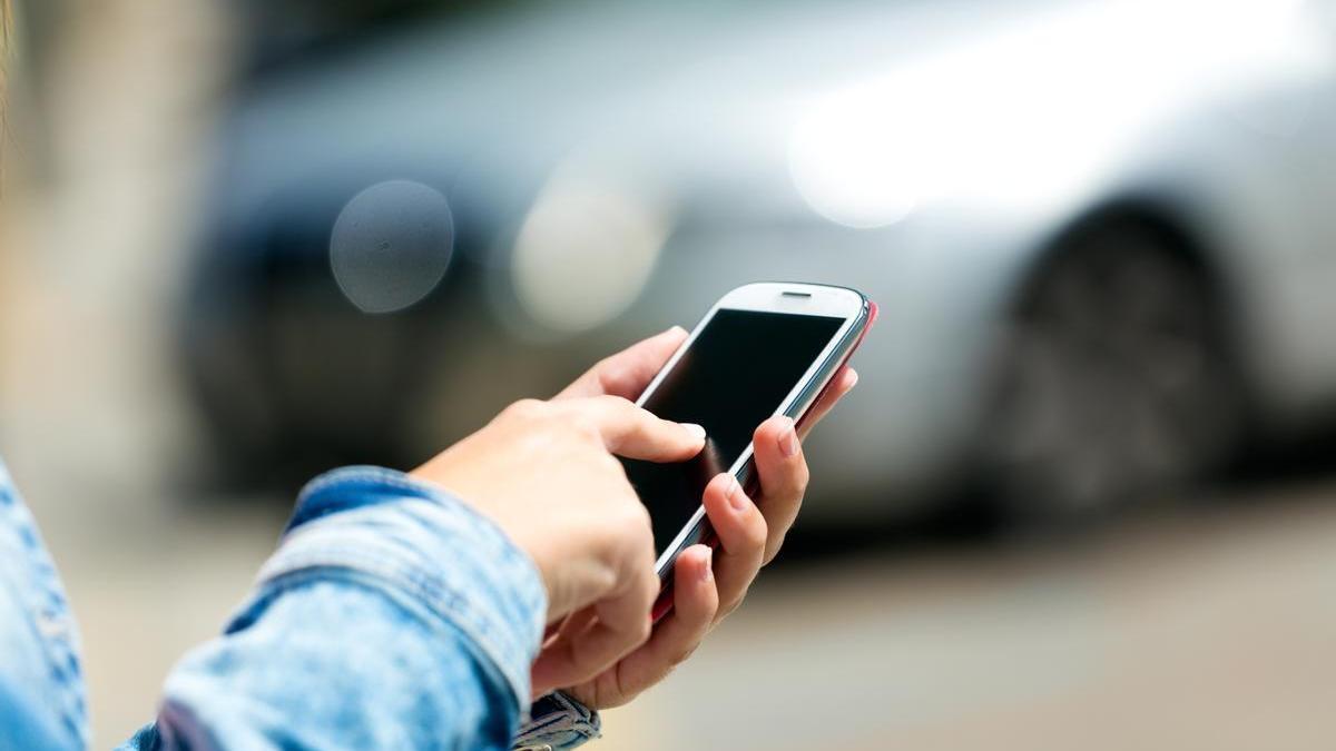 Mujer revisa su teléfono móvil para comprobar si puede abrir el coche a través de la aplicación móvil