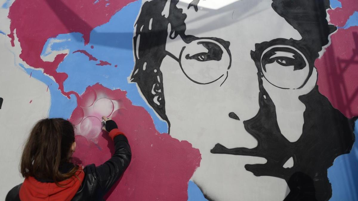 Una mujer pinta un mural de John Lennon.