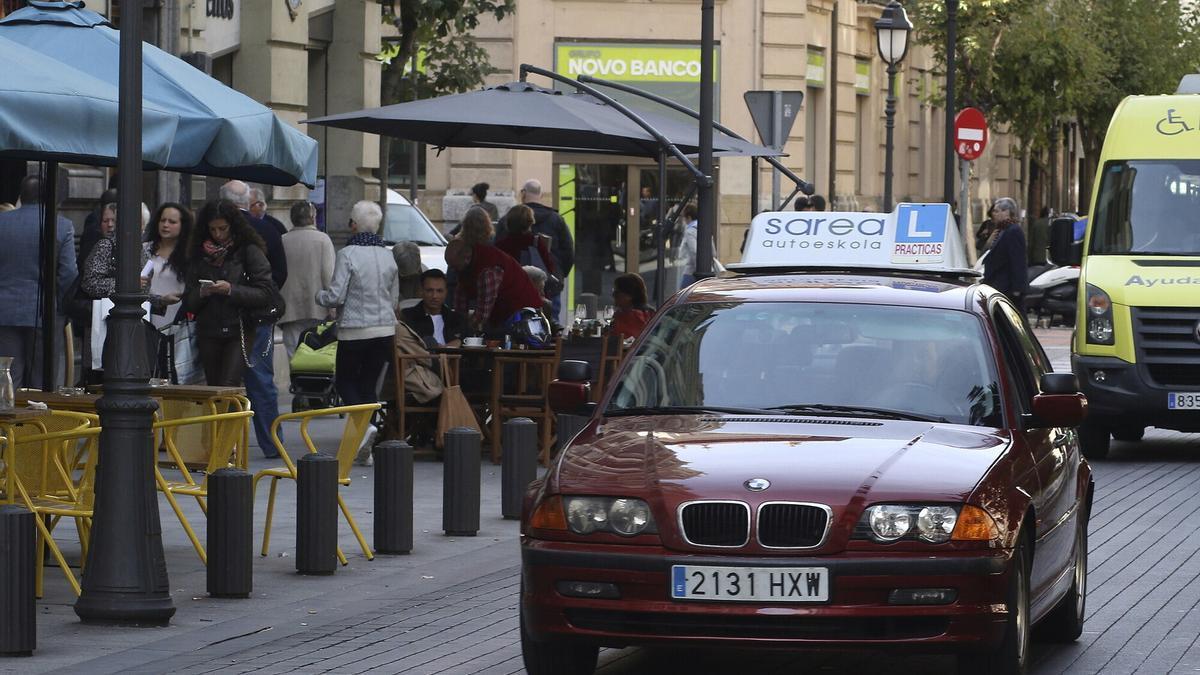 Un coche de prácticas circula por una calle concurrida.