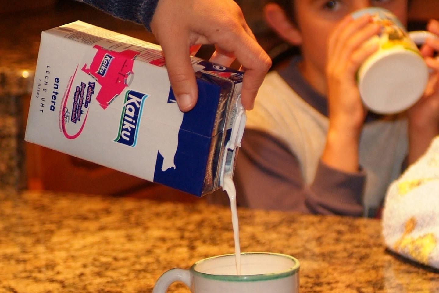 Una persona vierte leche Kaiku de un tetrabrick ante la mirada de un niño.