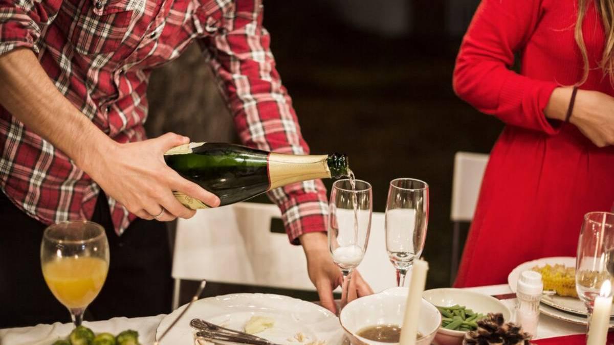 Hombre vierte champán en una copa en la mesa de Navidad