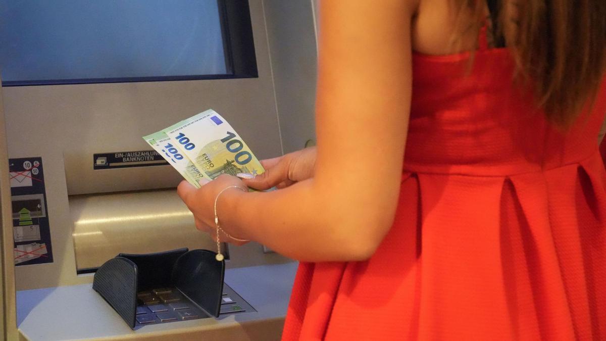 Una mujer sostiene unos billetes junto a un cajero automático.