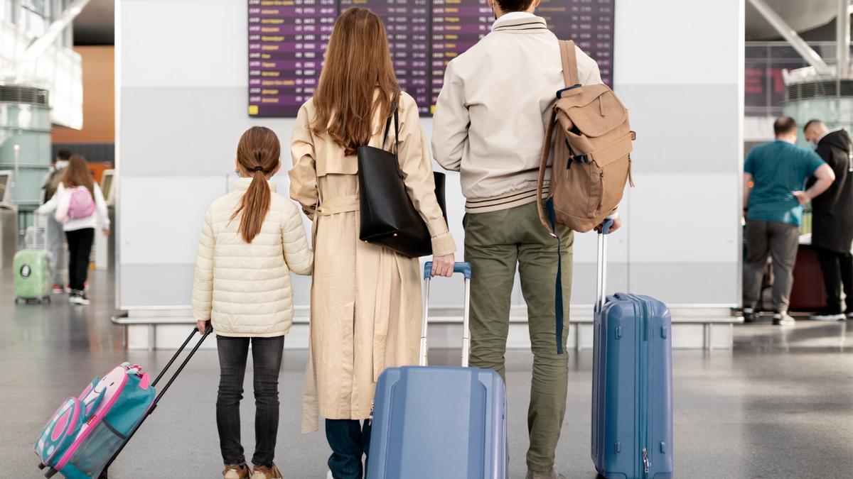 Unos pasajeros revisan su vuelo mientras sujetan las maletas
