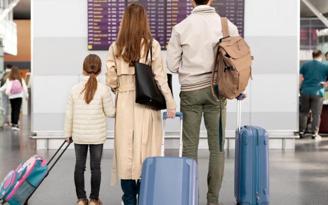 Unos pasajeros revisan su vuelo mientras sujetan las maletas
