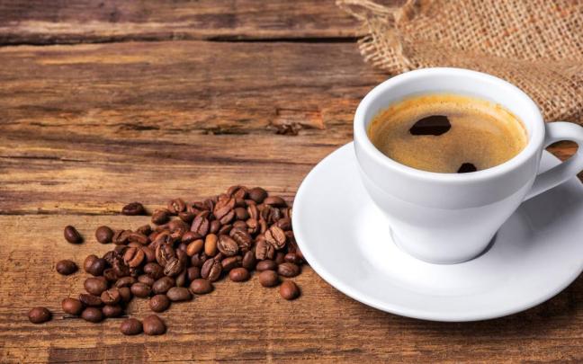 Una taza de café solo junto a un puñado de granos sin moler.