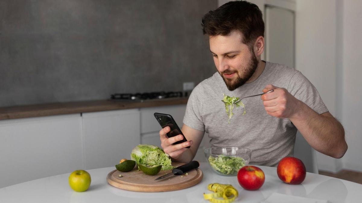 Un hombre come una ensalada mientras mira el móvil.