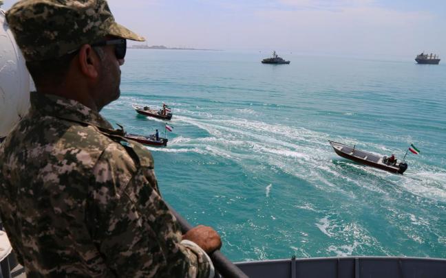 Un miembro de la Guardia Revolucionaria vigila mientras lanchas rápidas iraníes navegan por el Golfo Pérsico.