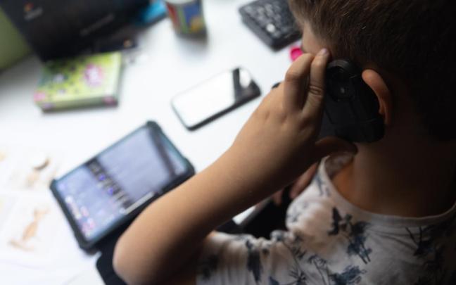 Un niño usa el teléfono móvil y una tablet.