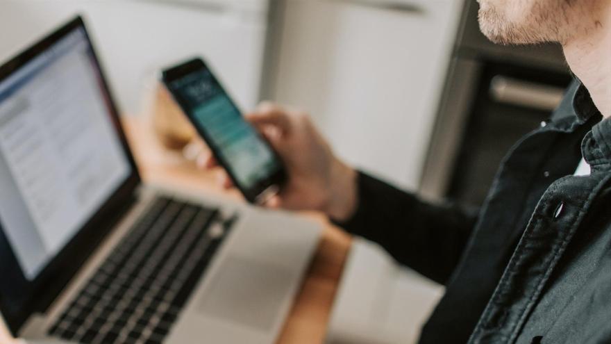 Un hombre utilizando un ordenador y un teléfono móvil.