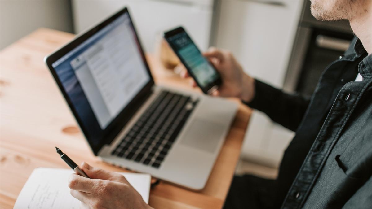 Un hombre utilizando un ordenador y un teléfono móvil.