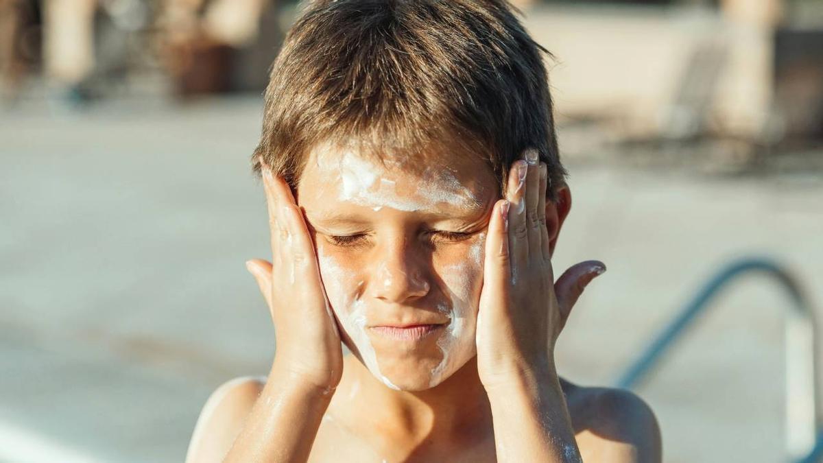 Un niño se aplica crema con protección solar en la cara.