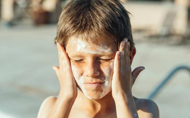Un niño se aplica crema con protección solar en la cara.