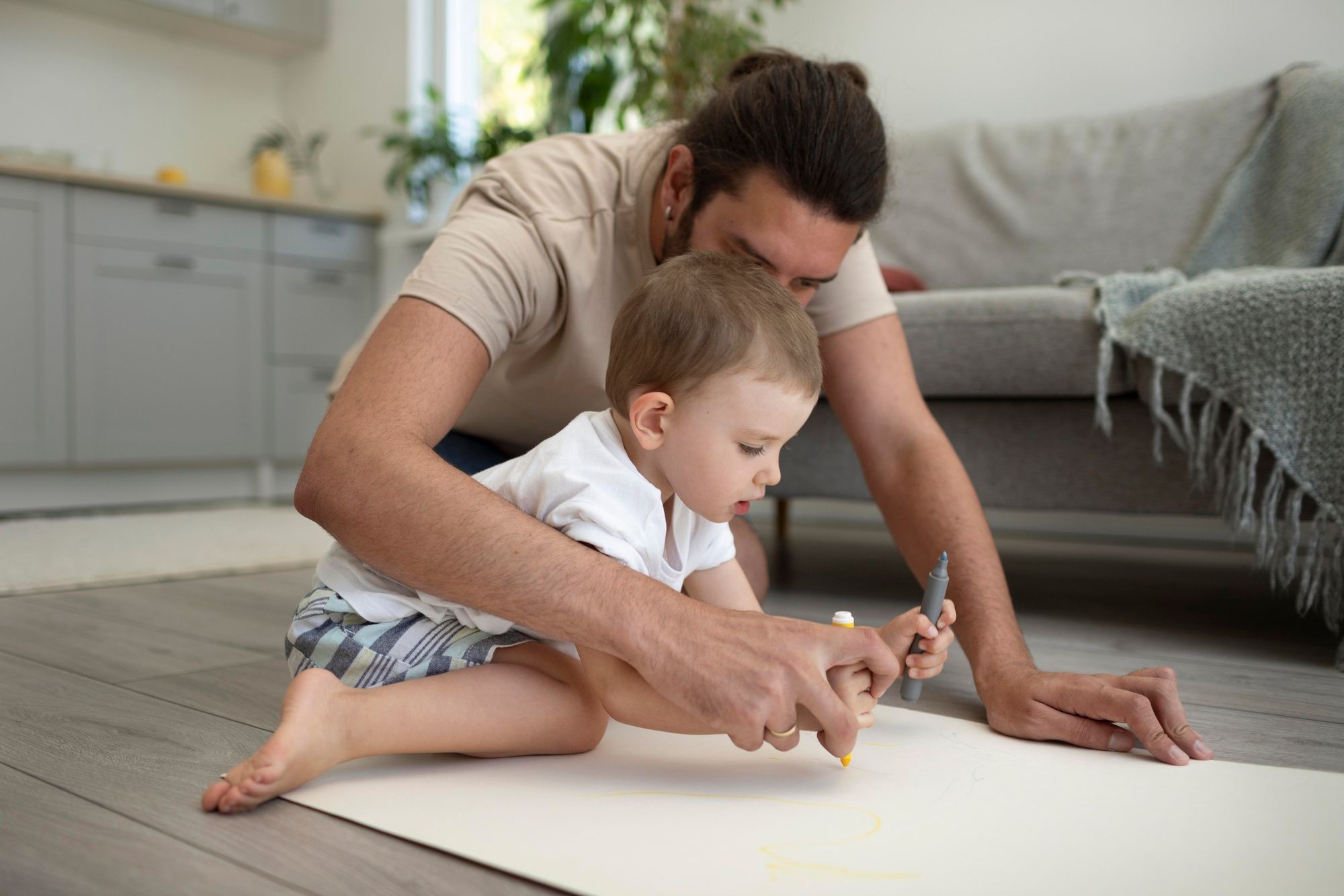 Un padre ayuda a su hijo a pintar sobre un cartón.