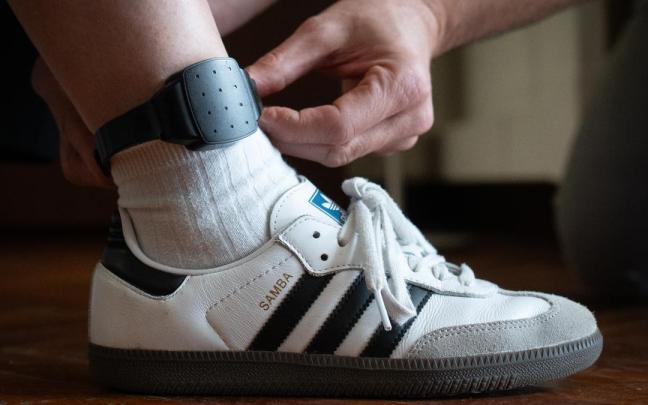 Una persona le coloca a otra una pulsera electrónica de geolocalización telemática.