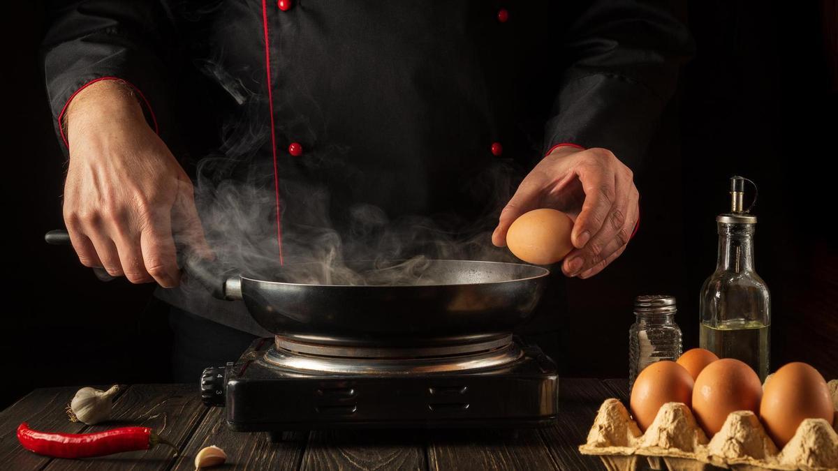 Un cocinero casca el huevo en el borde de la sartén donde lo va a freir.