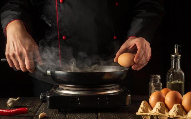 Un cocinero casca el huevo en el borde de la sartén donde lo va a freir. Un cocinero casca el huevo en el borde de la sartén donde lo va a freir.