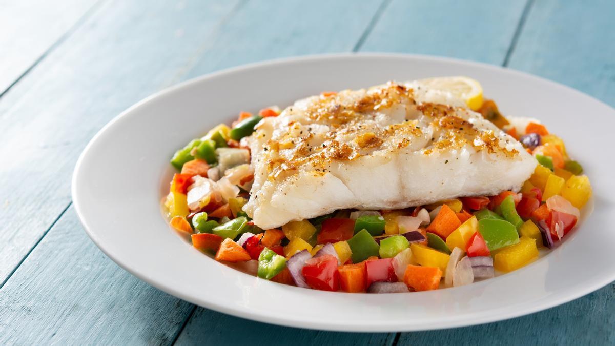 Un plato de pescado jugoso acompañado de verduras.