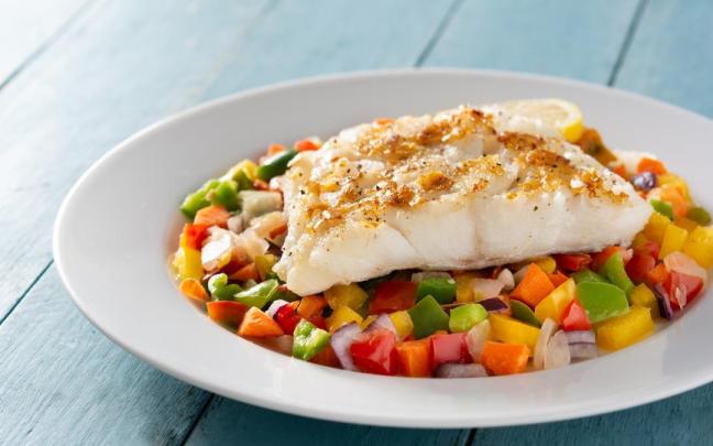 Un plato de pescado jugoso acompañado de verduras.