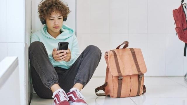 Estudiante sentado suelo usando teléfono móvil