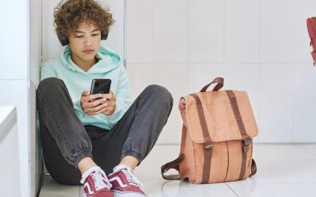 Estudiante sentado suelo usando teléfono móvil