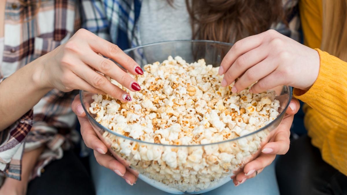 Dos personas cogiendo palomitas de un recipiente. FREEPIK